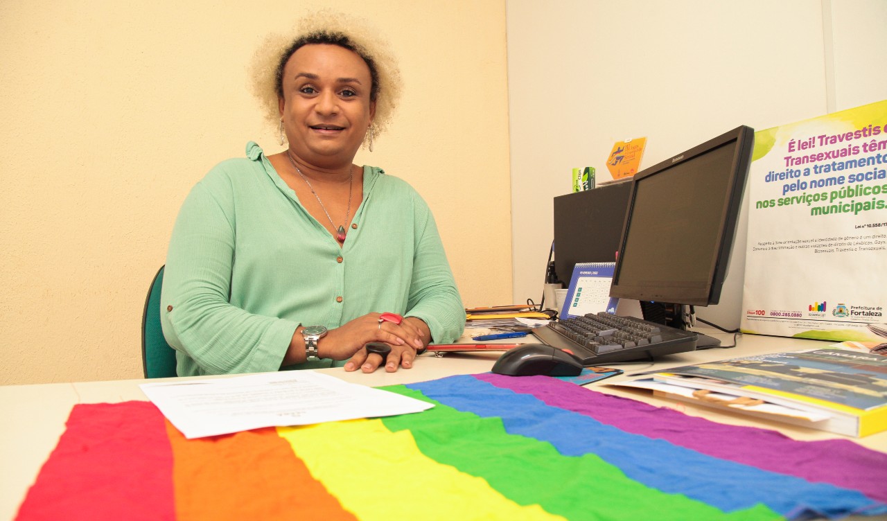 labelle posa para a foto em sua sala de trabalho com uma bandeira LGBT